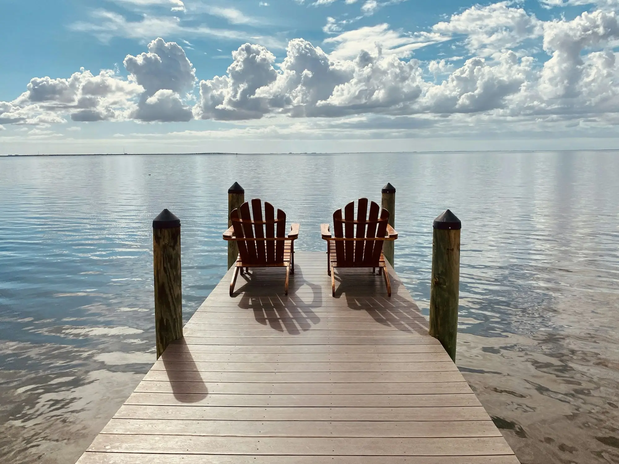 Two chairs at the end of a wooden dock on calm water