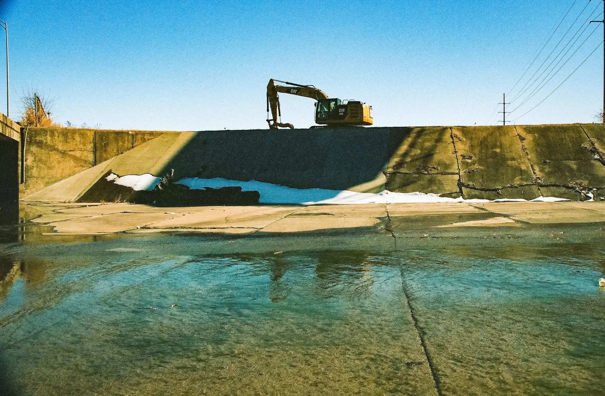 An excavator working on top of a concrete wall by the water